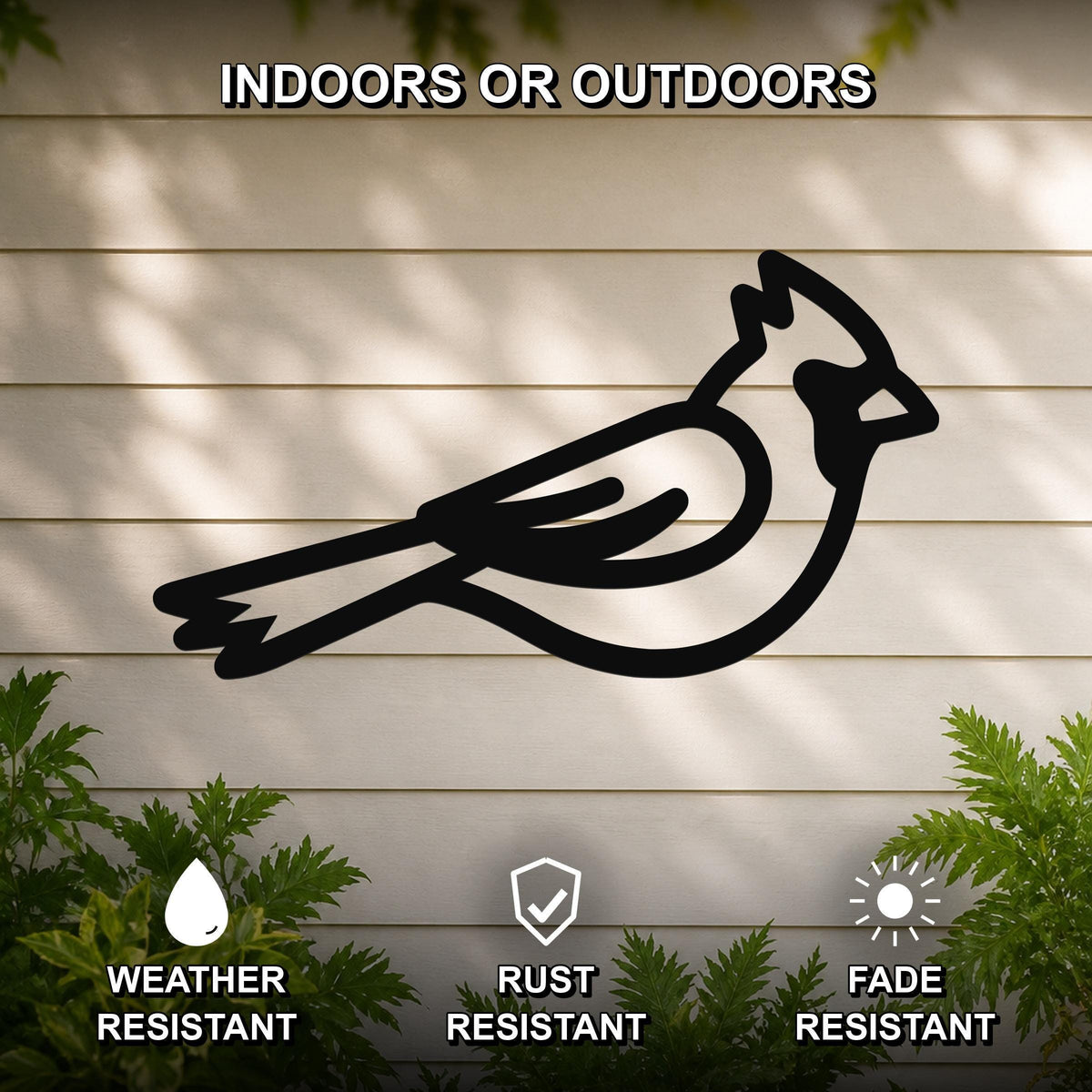 Black metal cardinal wall art silhouette mounted on a light-colored outdoor wall, with green foliage at the bottom and text indicating it is weather, rust, and fade resistant.