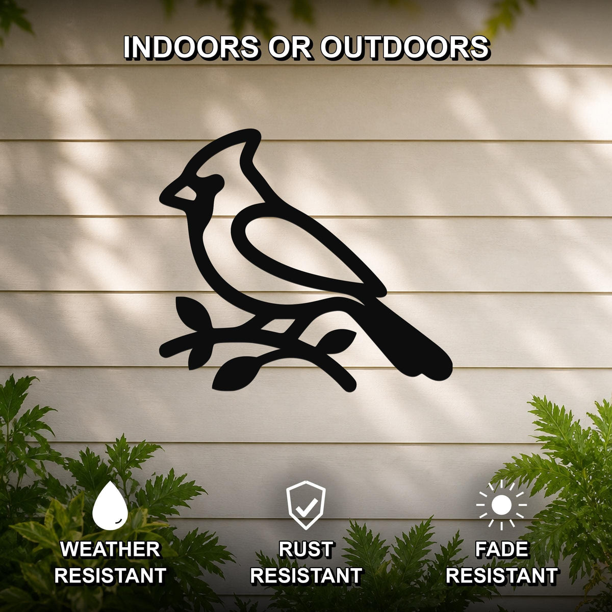 Black metal cardinal wall art silhouette perched on a branch, mounted on a light-colored outdoor wall with greenery, weather resistant, rust resistant, and fade resistant.