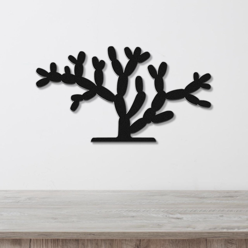 Black metal wall art cutout of a cholla cactus with branching arms, mounted on a white wall above a light wood surface.