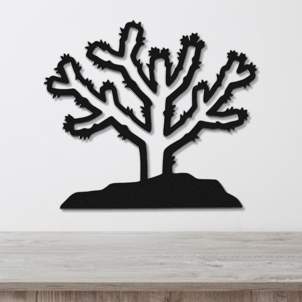 Black metal wall art cutout of a cholla cactus with branching arms and spines, mounted on a white wall above a light wood surface.