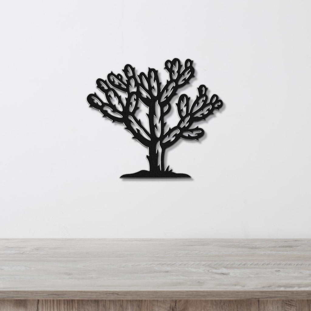 Black metal wall art cutout of a cholla cactus with detailed branching arms, mounted on a white wall above a light wood surface.