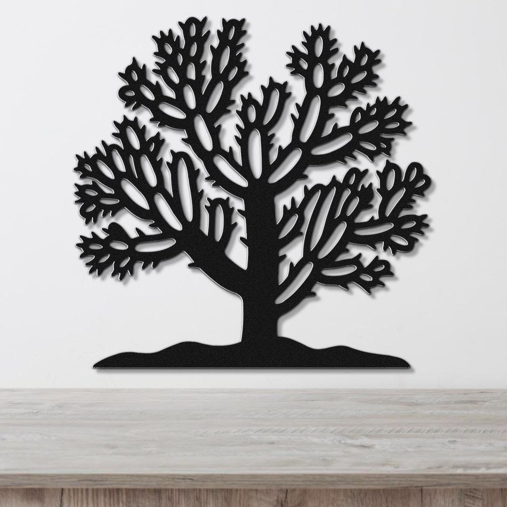 Black metal wall art featuring a bold cholla cactus silhouette with intricate branch cutouts, mounted on a white wall above a light wood surface.