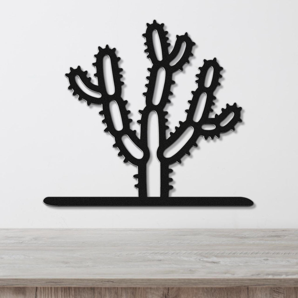 Black metal Cholla cactus wall art with spiny branch cutouts, mounted on a white wall above a wooden counter.