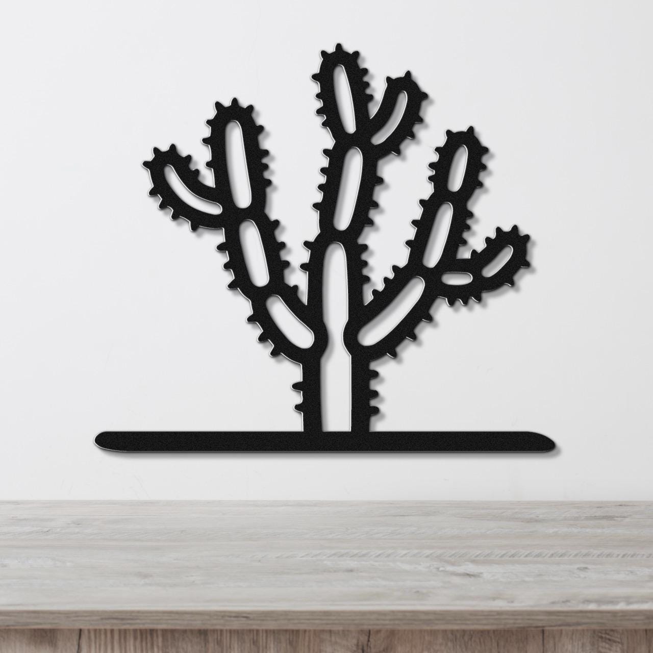 Black metal Cholla cactus wall art with spiny branch cutouts, mounted on a white wall above a wooden counter.