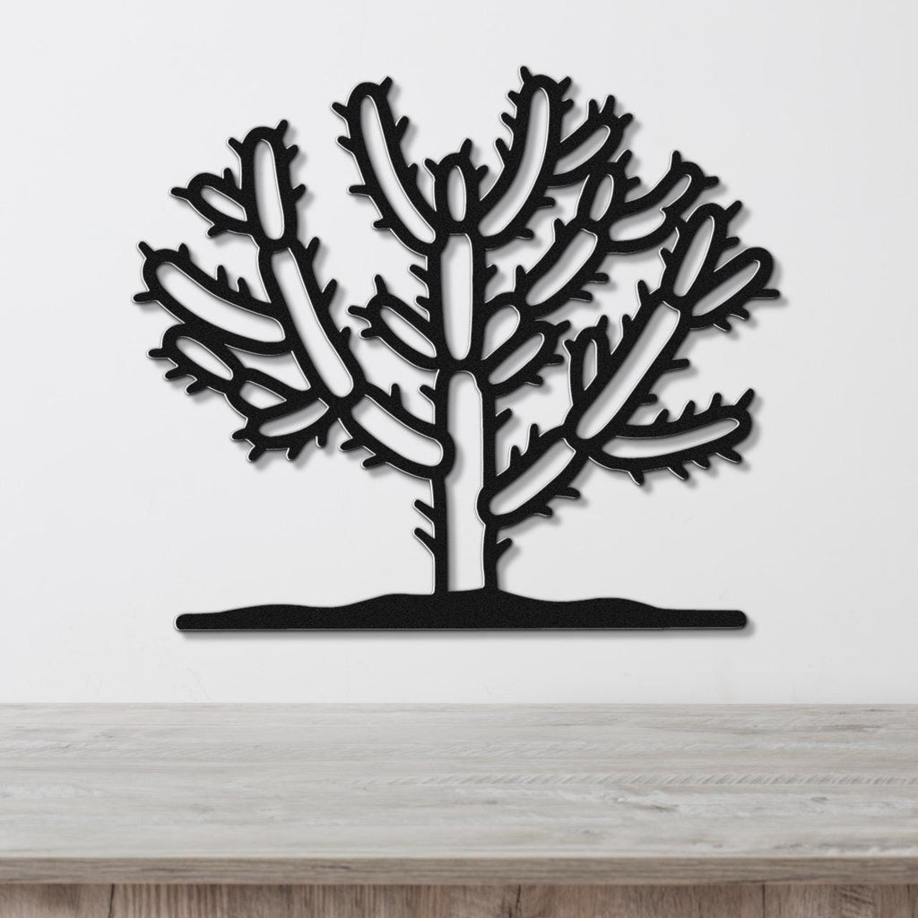 Black metal wall art cutout of a cholla cactus with branching arms and spines, mounted on a white wall above a light wood surface.
