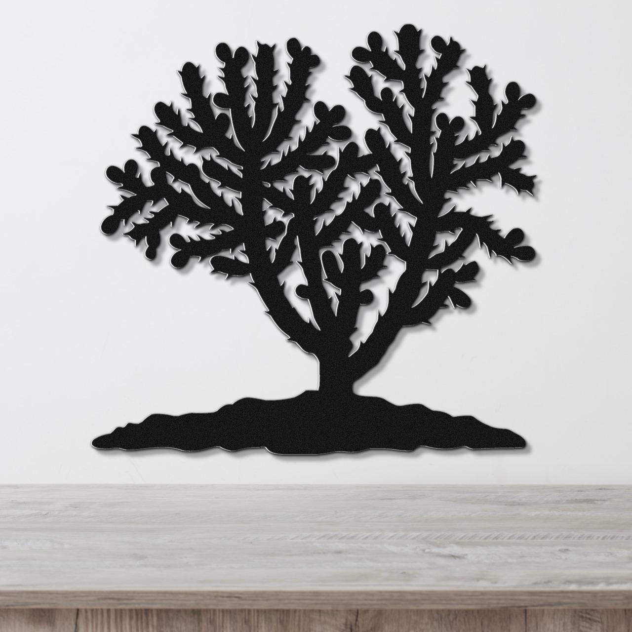 Black metal wall art cutout of a cholla cactus with branching arms and spines, mounted on a white wall above a light wood counter.