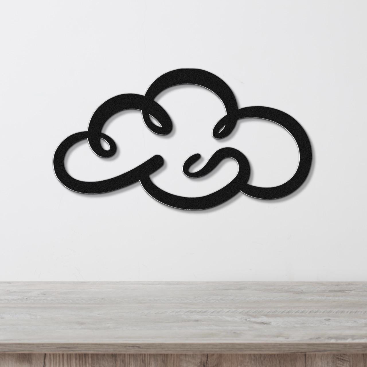 Black metal cloud wall art with a cutout design, mounted on a white wall above a light wood surface.