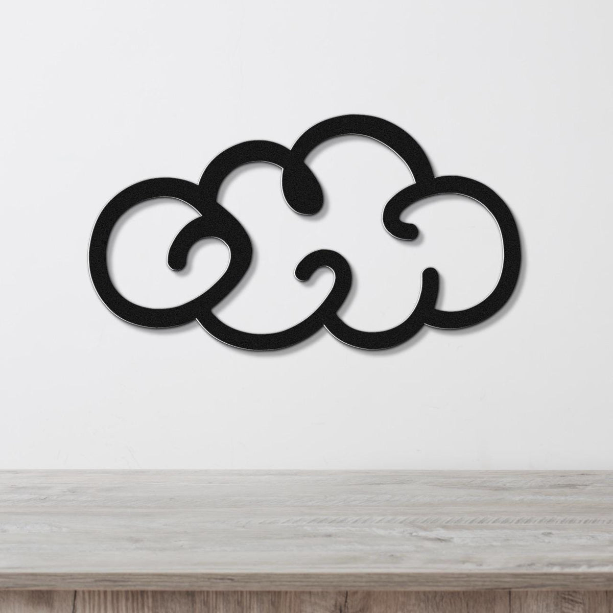 Black metal cloud wall art with a cutout design, mounted on a white wall above a wooden surface.