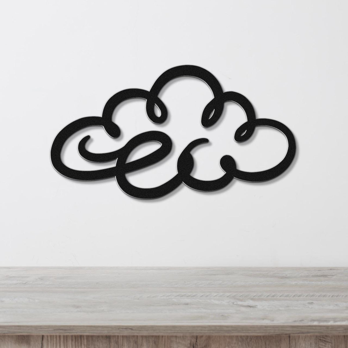 Black metal cloud wall art with flowing silhouette cutouts, mounted on a white wall above a light wood surface.