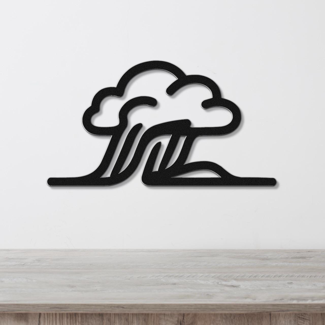 Black metal wall art with a cloud and wave silhouette design, mounted on a white wall above a light wood surface.