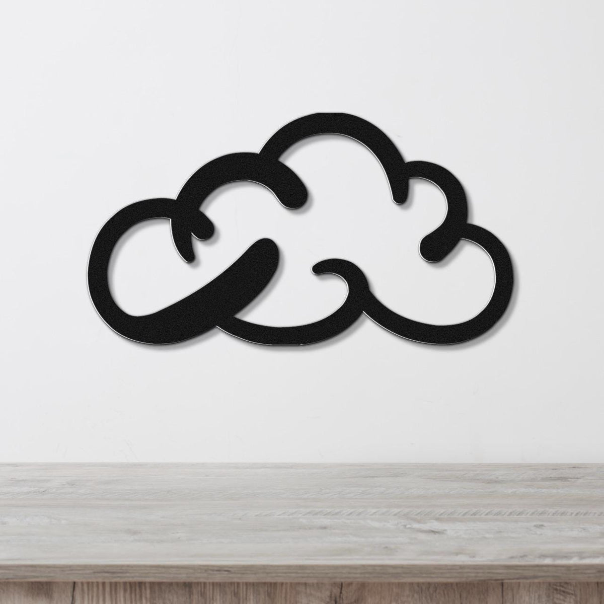 Black metal cloud-shaped wall art with internal cutout details, mounted on a white wall above a light wood surface.