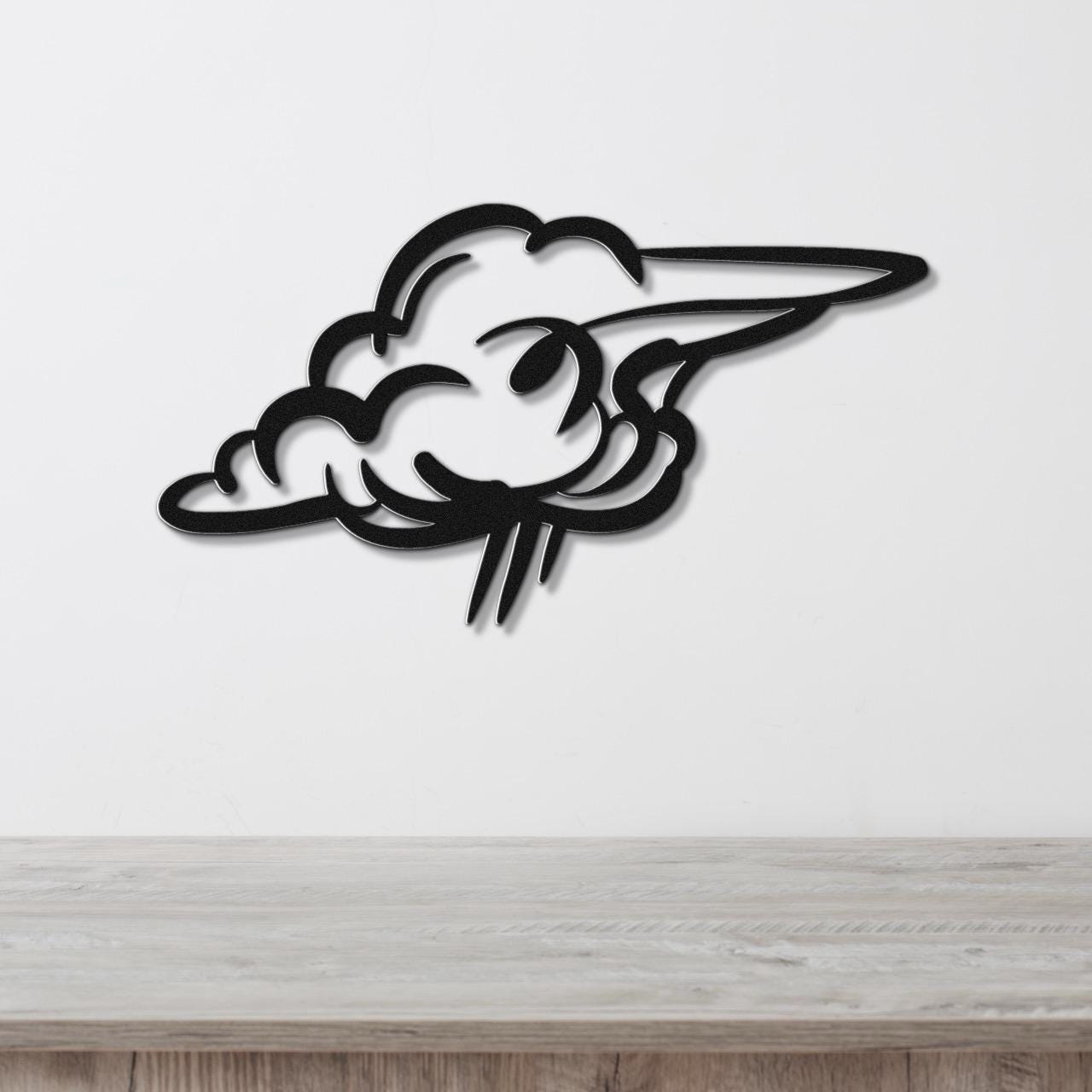 Black metal cloud wall art with a cutout design, mounted on a white wall above a wooden surface.