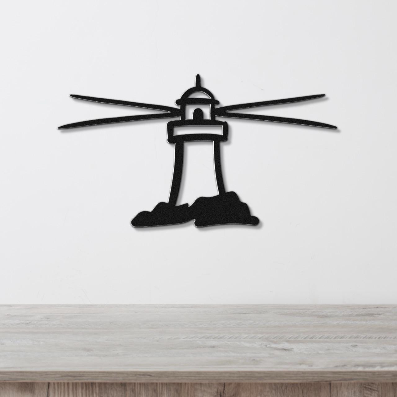 Black metal lighthouse wall art with radiating beam cutouts, mounted on a white wall above a light wood surface.