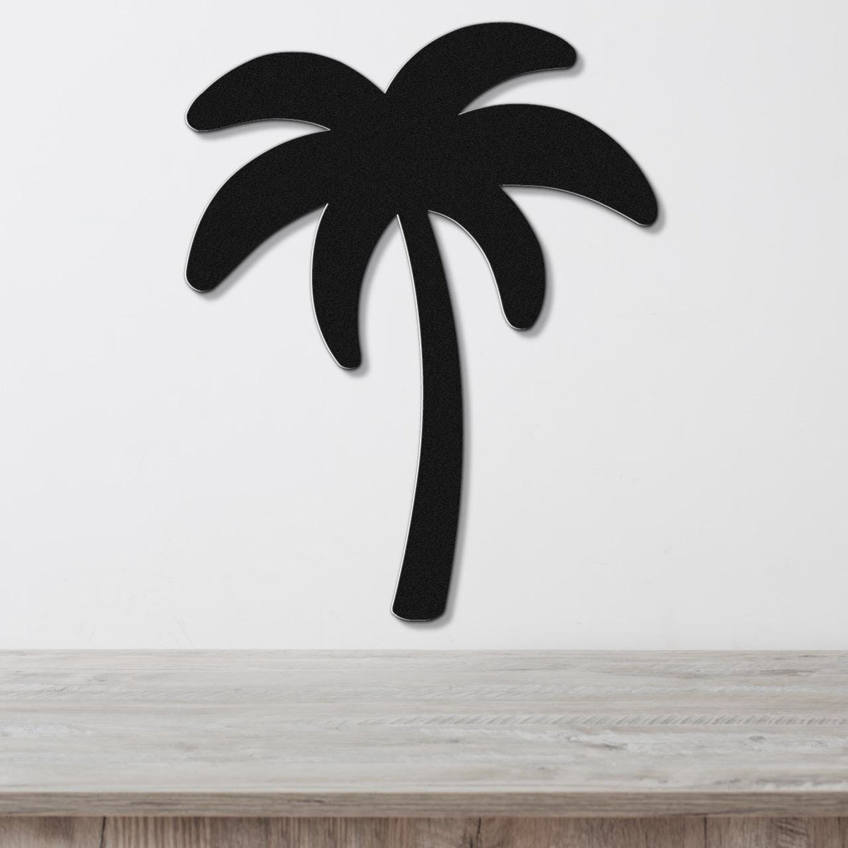 Black metal palm tree wall art with a silhouette design, mounted on a white wall above a light wood surface.