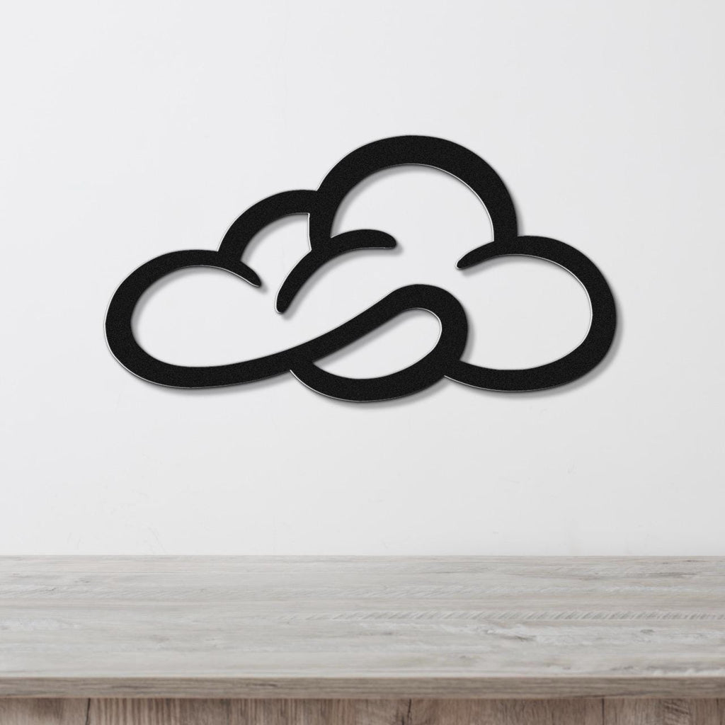 Black metal cloud wall art with open silhouette cutouts, mounted on a white wall above a light wood surface.