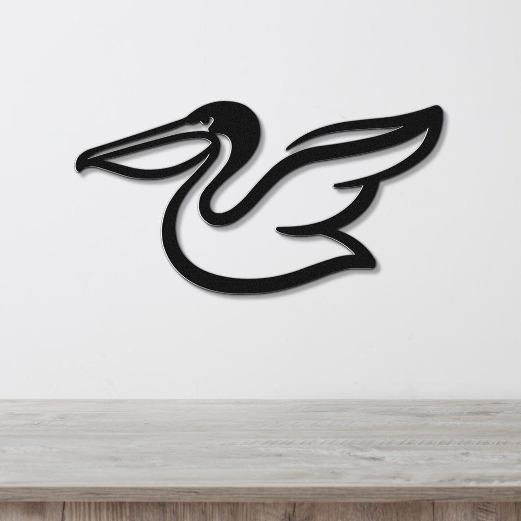Black metal pelican wall art with a sleek silhouette and wing cutout, mounted on a white wall above a light wood surface.