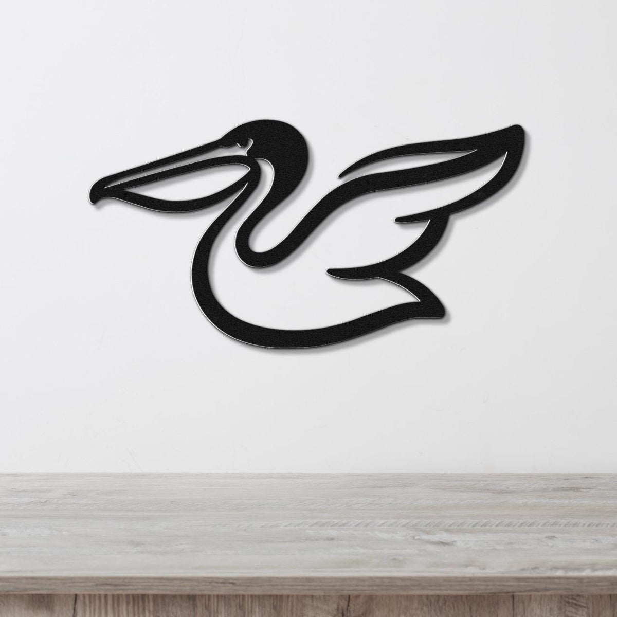 Black metal pelican wall art with a sleek silhouette and wing cutout, mounted on a white wall above a light wood surface.