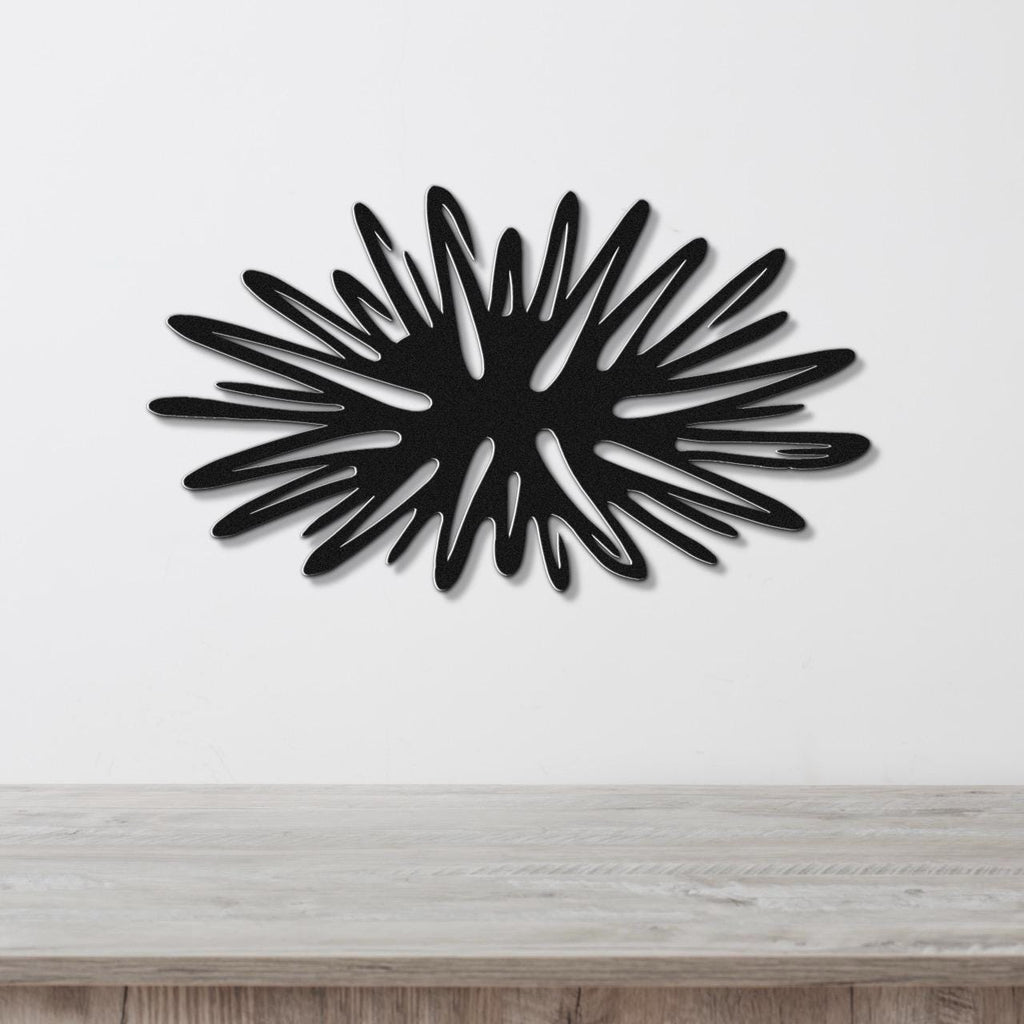Black metal sea urchin wall art with radiating spines and internal cutouts, mounted on a white wall above a light wood surface.
