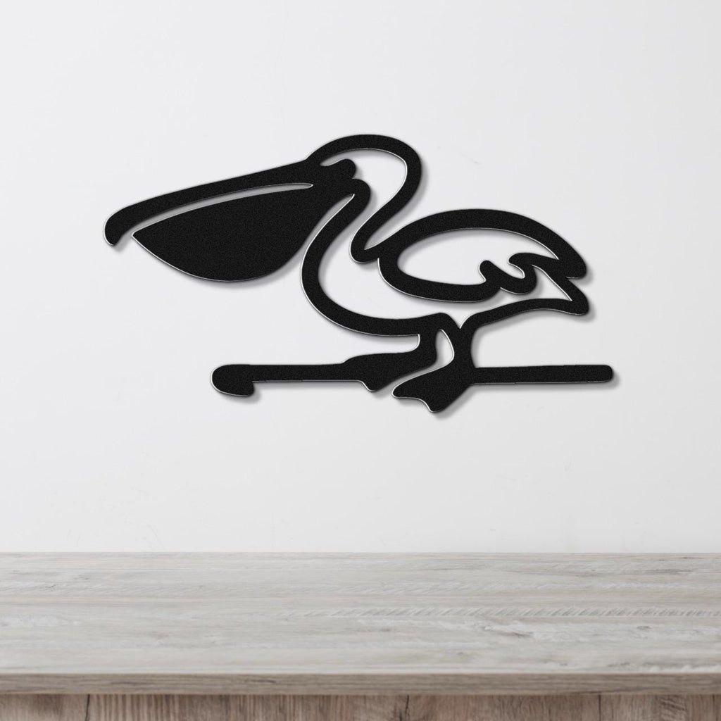 Black metal pelican wall art with a cutout silhouette design, mounted on a white wall above a light wood surface.
