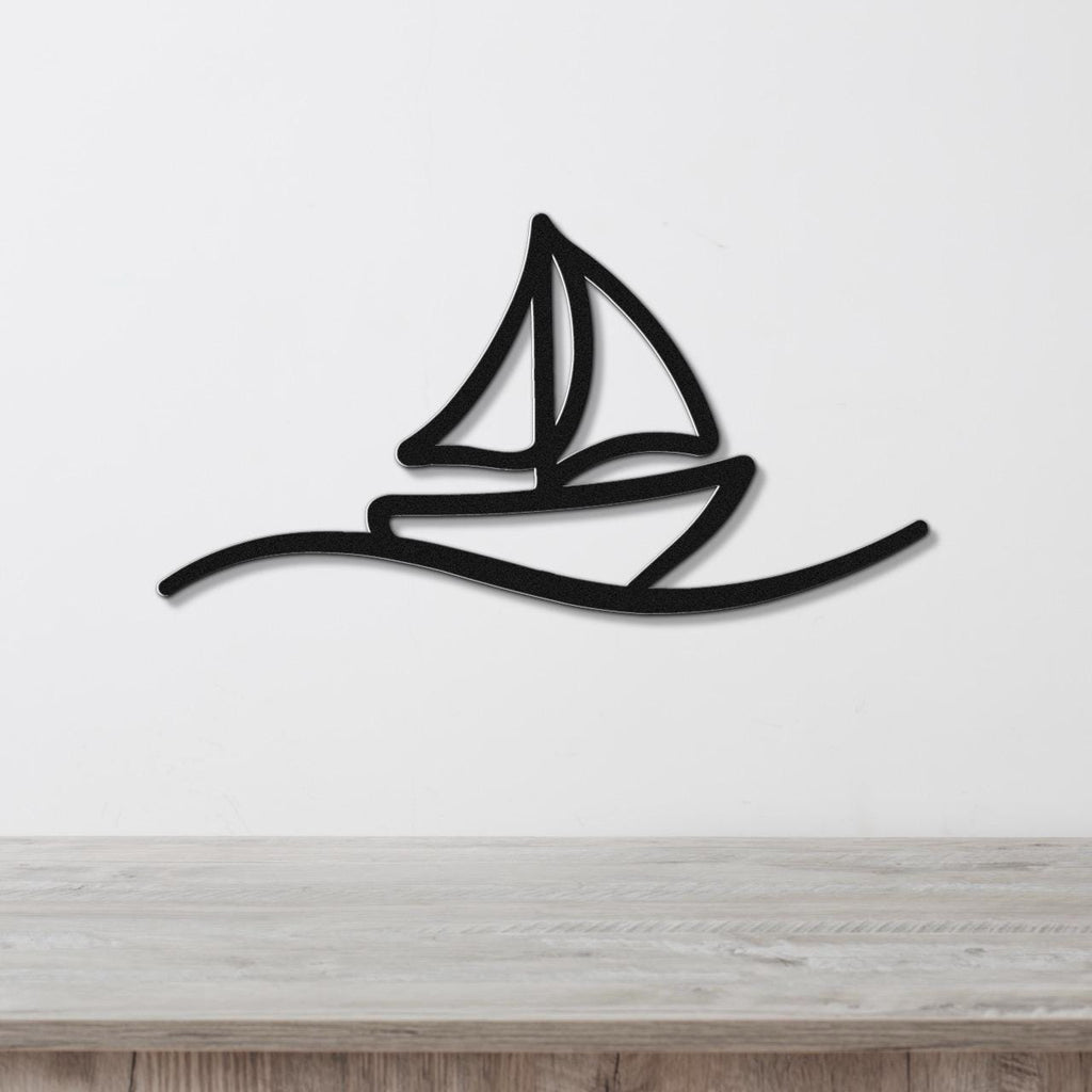 Black metal sailboat wall art with a silhouette design and wave cutout, mounted on a white wall above a wooden surface.
