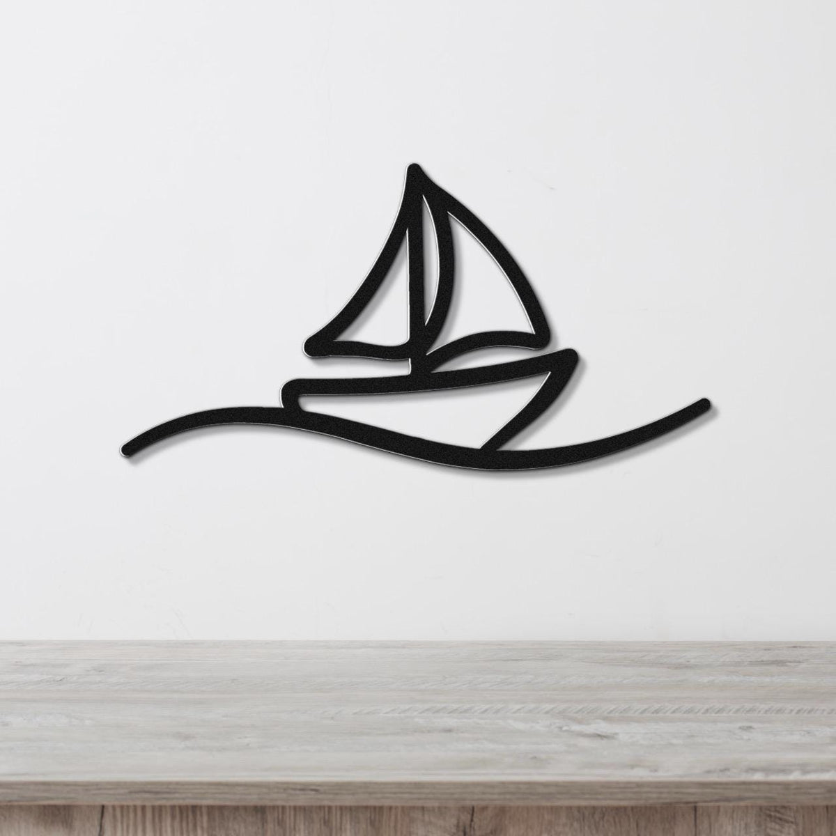 Black metal sailboat wall art with a silhouette design and wave cutout, mounted on a white wall above a wooden surface.