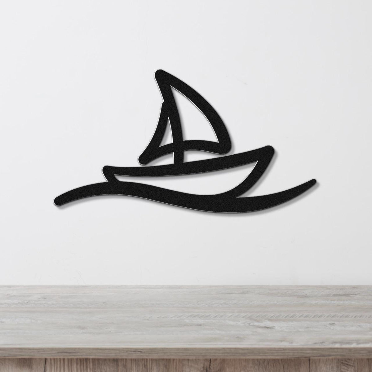 Black metal wall art in a sailboat silhouette with a cutout sail and wave design, mounted on a white wall above a wooden surface.