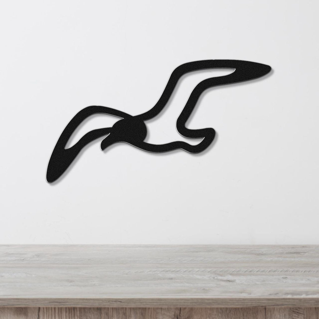 Black metal seagull wall art with a cutout silhouette design, mounted on a white wall above a light wood surface.
