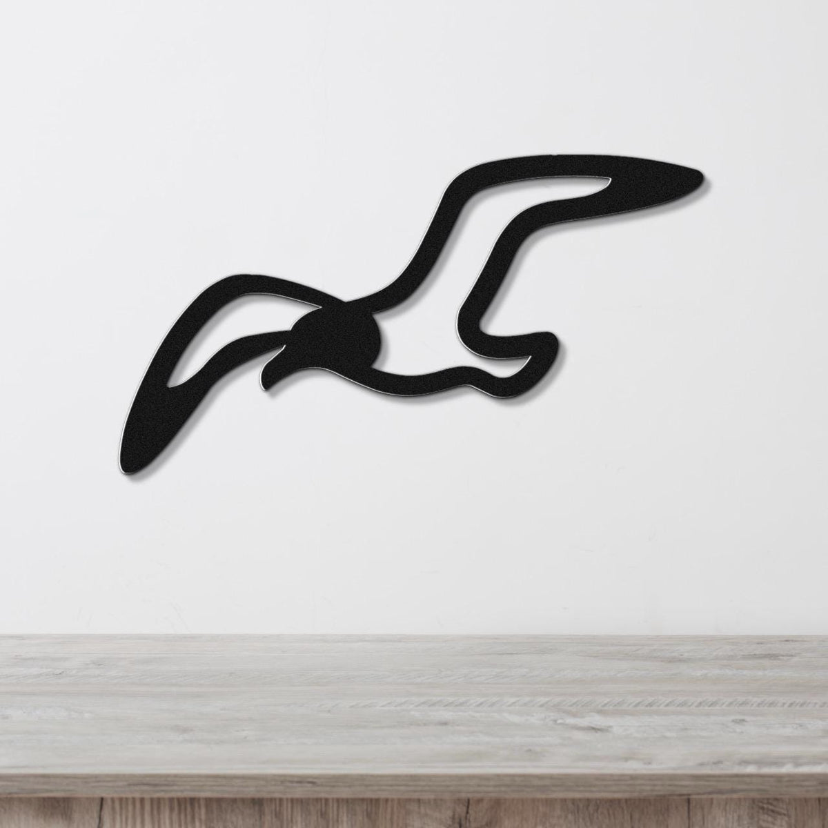 Black metal seagull wall art with a cutout silhouette design, mounted on a white wall above a light wood surface.