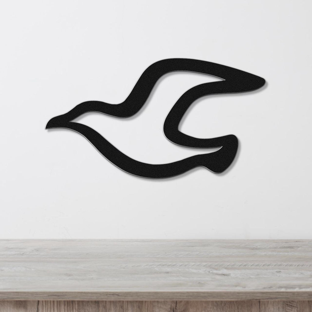 Black metal seagull wall art with flowing wing cutouts, mounted on a white wall above a light wood countertop.