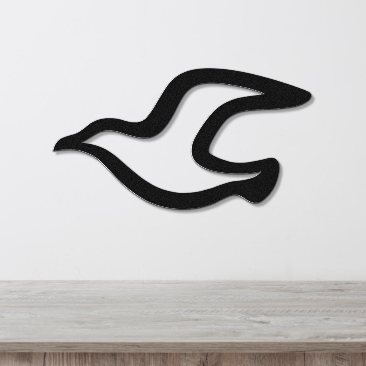 Black metal seagull wall art with flowing wing cutouts, mounted on a white wall above a light wood countertop.