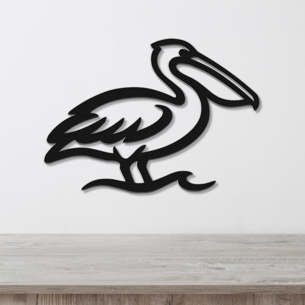 Black metal pelican wall art with a cutout silhouette design, mounted on a white wall above a light wood surface.