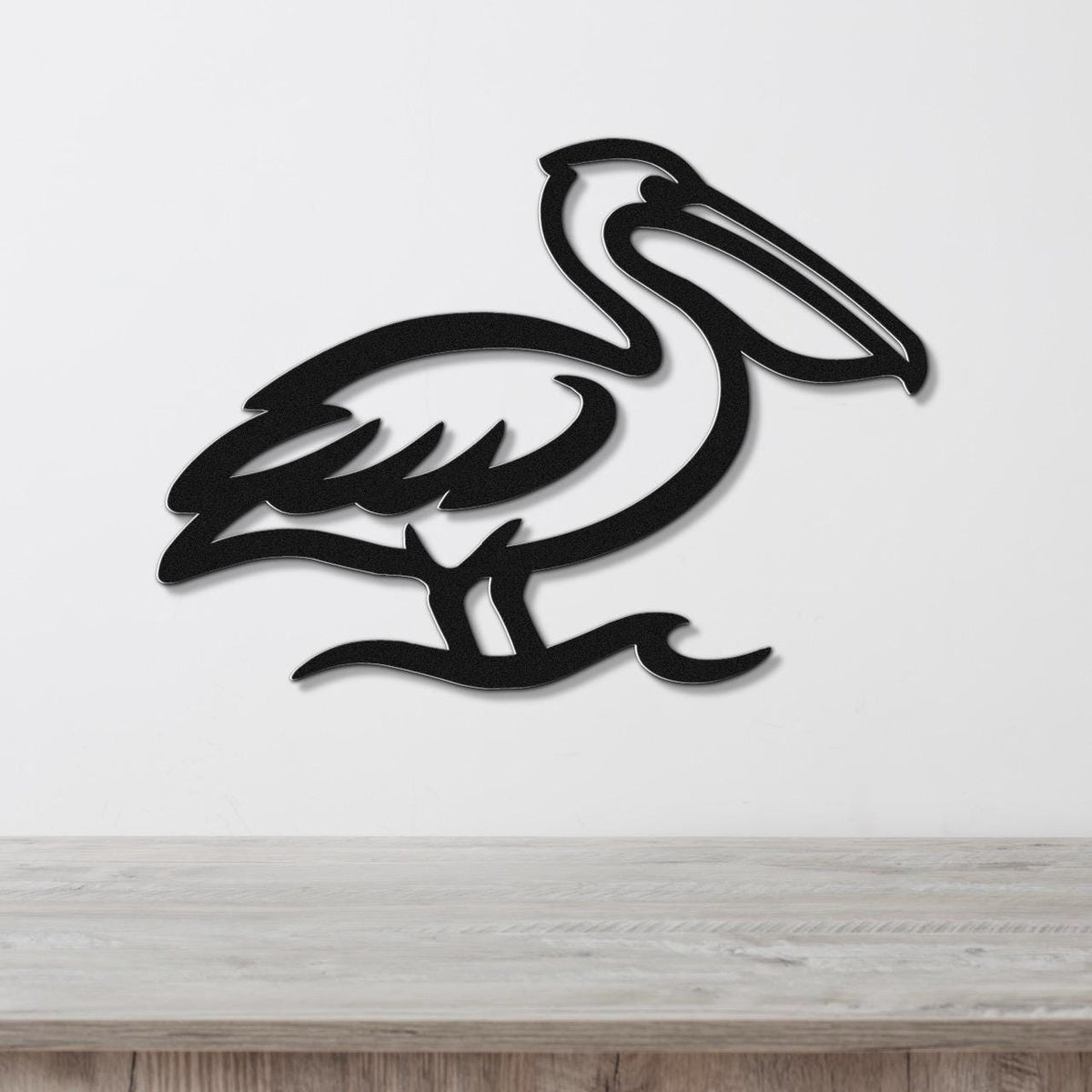 Black metal pelican wall art with a cutout silhouette design, mounted on a white wall above a light wood surface.