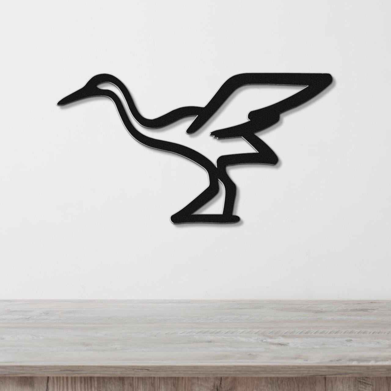 Black metal crane wall art with a minimalist silhouette design, mounted on a white wall above a light wood surface.