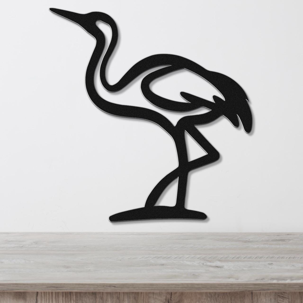 Black metal crane wall art with a minimalist silhouette design, mounted on a white wall above a light wood surface.