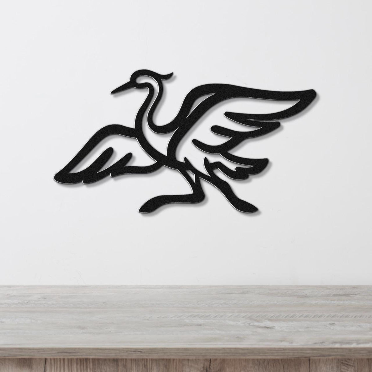 Black metal crane wall art with wing and leg cutouts, mounted on a white wall above a light wood surface.