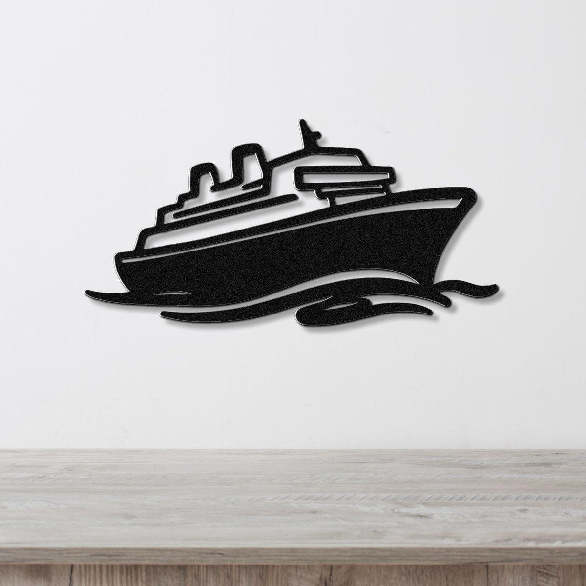 Black metal wall art cutout of a cruise ship with wave motion lines, mounted on a white wall above a wooden surface.