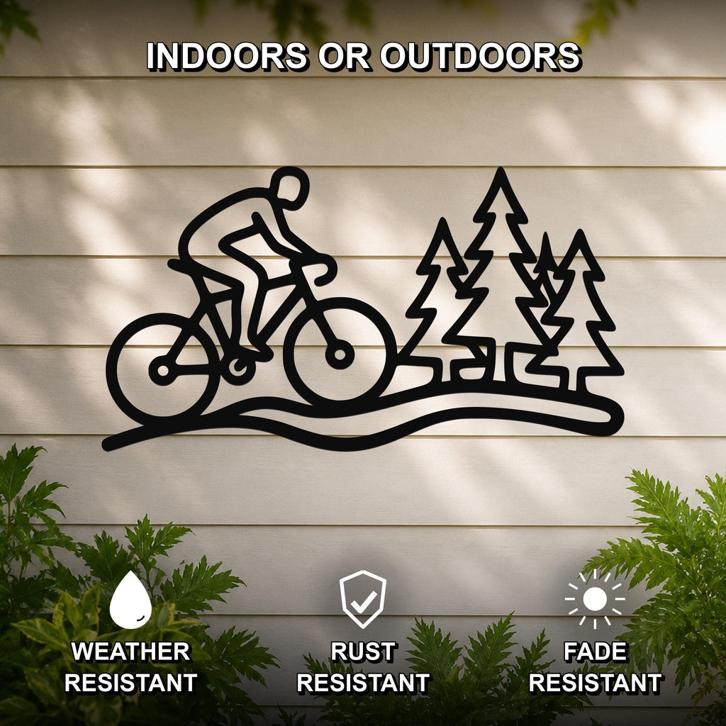 Black metal wall art featuring a cyclist silhouette on a trail with pine trees, mounted on a light-colored outdoor wall with greenery below.