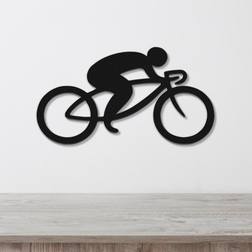 Black metal wall art featuring a minimalist cyclist silhouette in a racing pose, mounted on a white wall above a light wood surface.