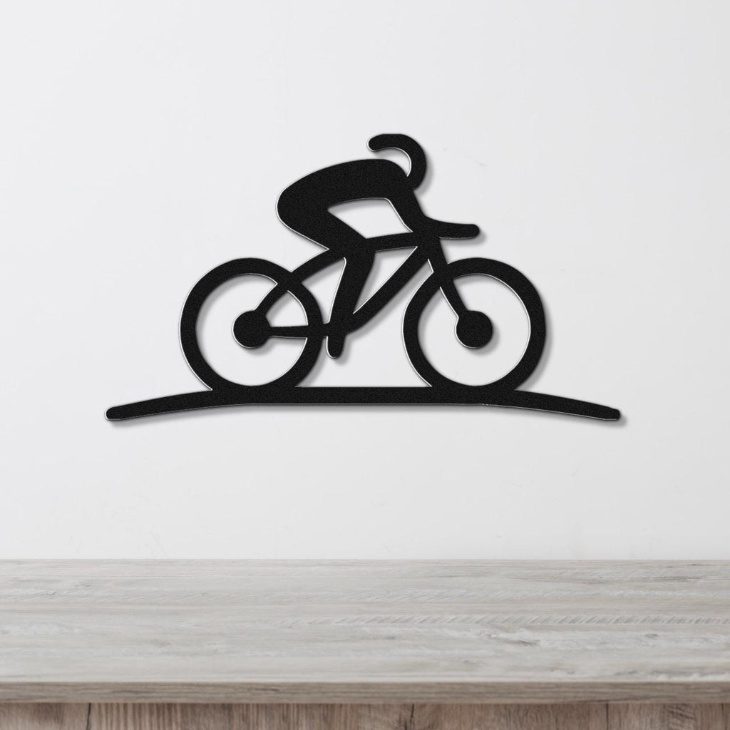 Black metal wall art silhouette of a cyclist on a bike, mounted on a white wall above a wooden surface.
