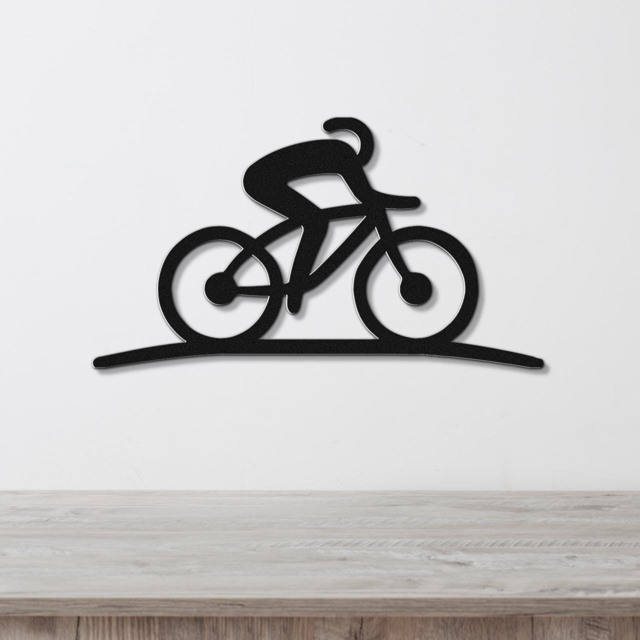 Black metal wall art silhouette of a cyclist on a bike, mounted on a white wall above a wooden surface.