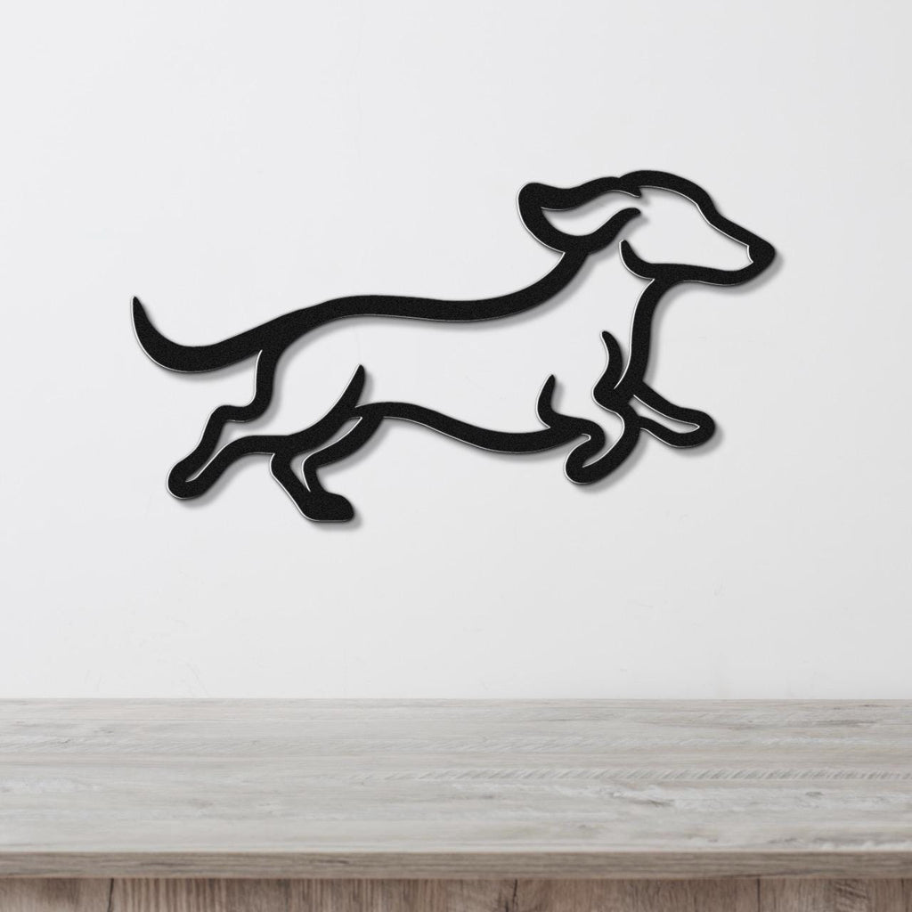 Black metal wall art in the silhouette of a running dachshund, mounted on a white wall above a light wood surface.