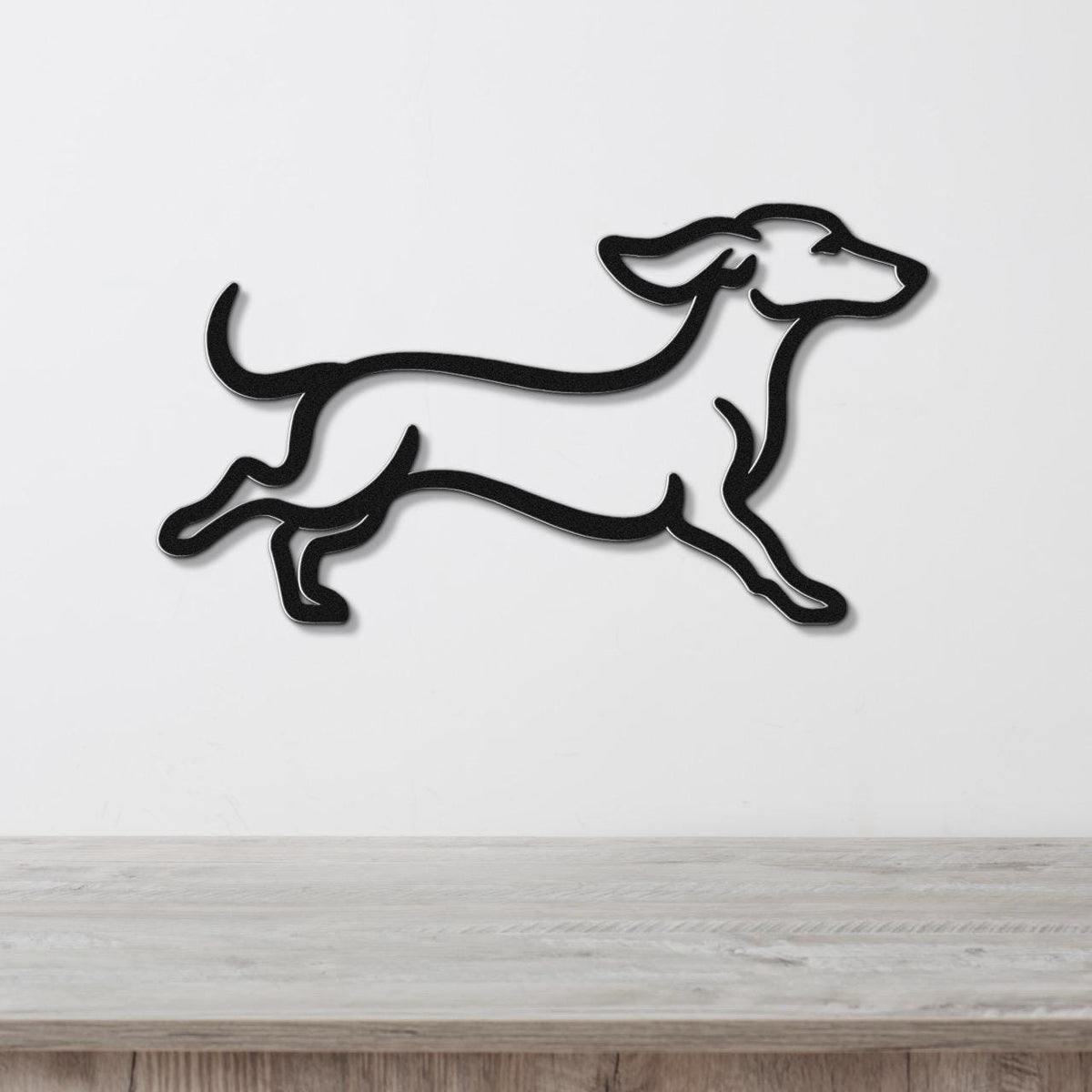 Black metal dachshund wall art in a running silhouette, mounted on a white wall above a light wood counter.