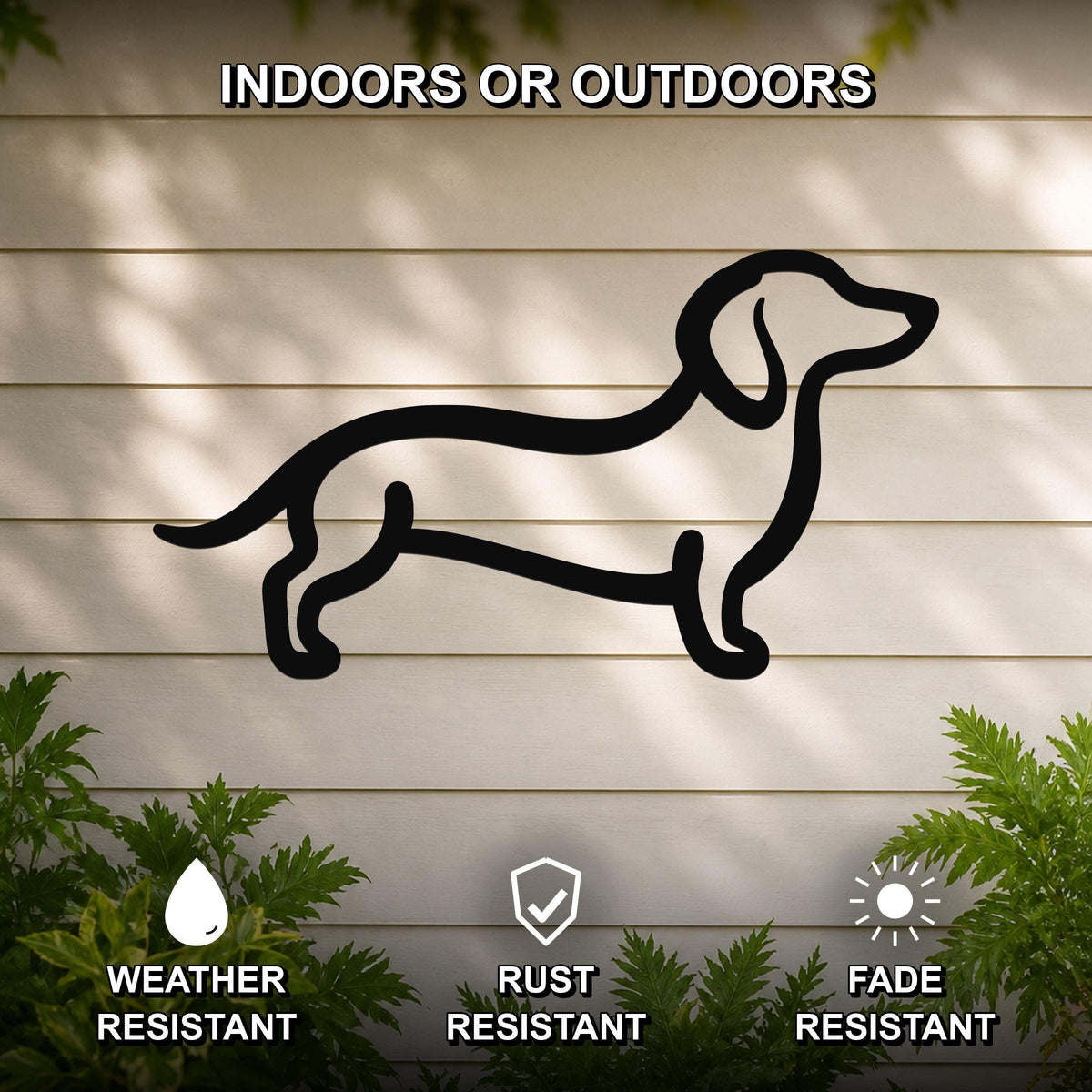 Black metal dachshund silhouette wall art mounted on a light-colored outdoor wall, with green plants at the base and text indicating it is weather, rust, and fade resistant.