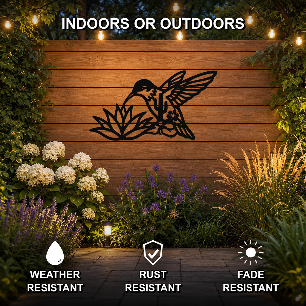 Black metal hummingbird wall art with flower and leaf cutouts, mounted on a wooden outdoor wall above a garden with string lights and plants.