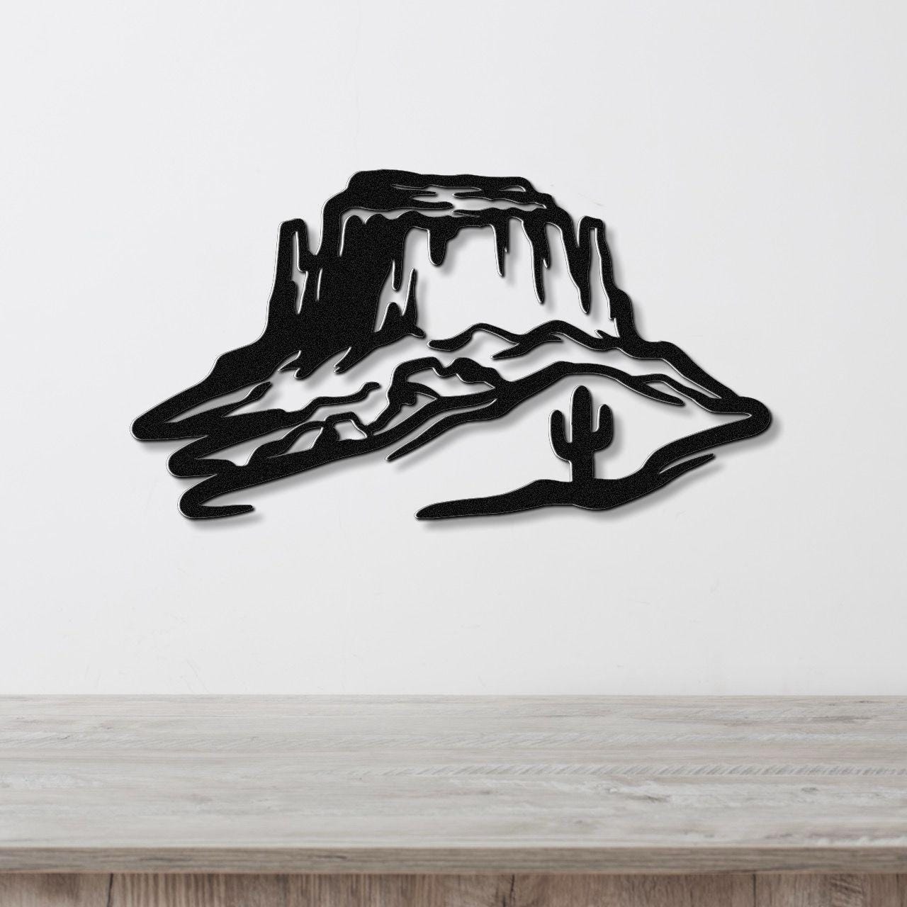 Black metal wall art silhouette of a desert mesa with a saguaro cactus, mounted on a white wall above a wooden counter.