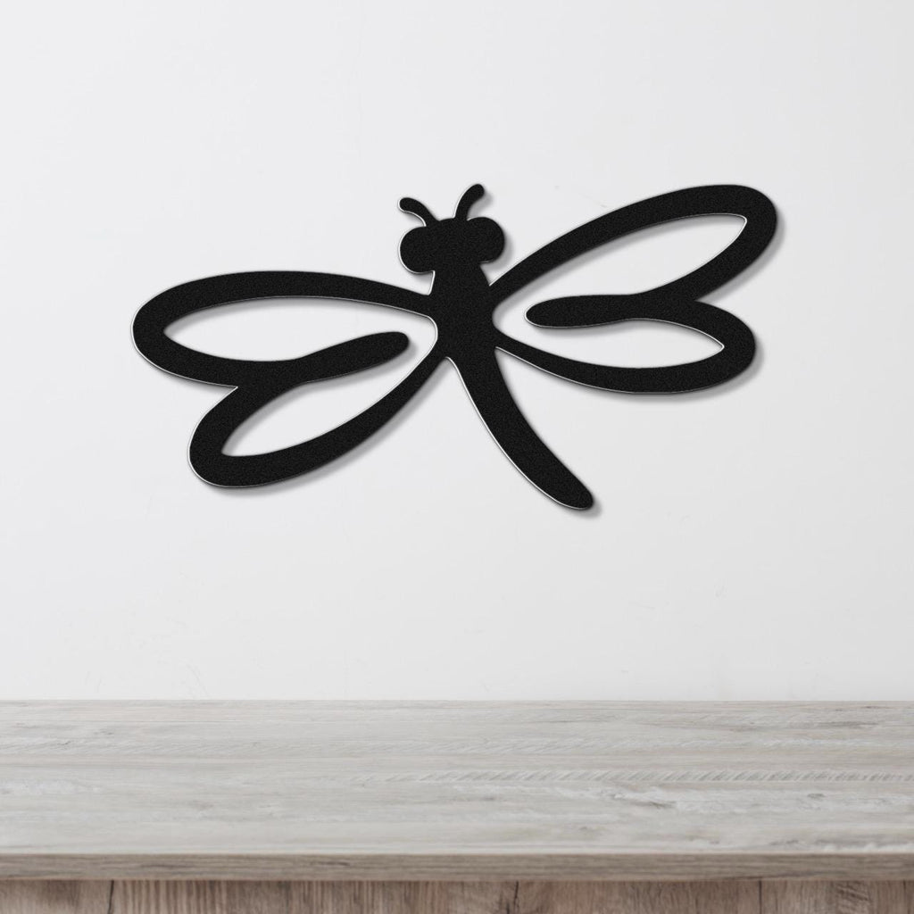 Black metal dragonfly wall art with cutout wings and body, mounted on a white wall above a light wood surface.