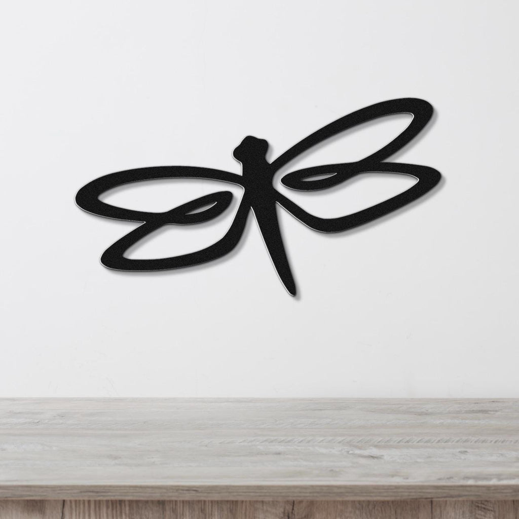 Black metal dragonfly wall art with flowing wing cutouts, mounted on a white wall above a light wood surface.