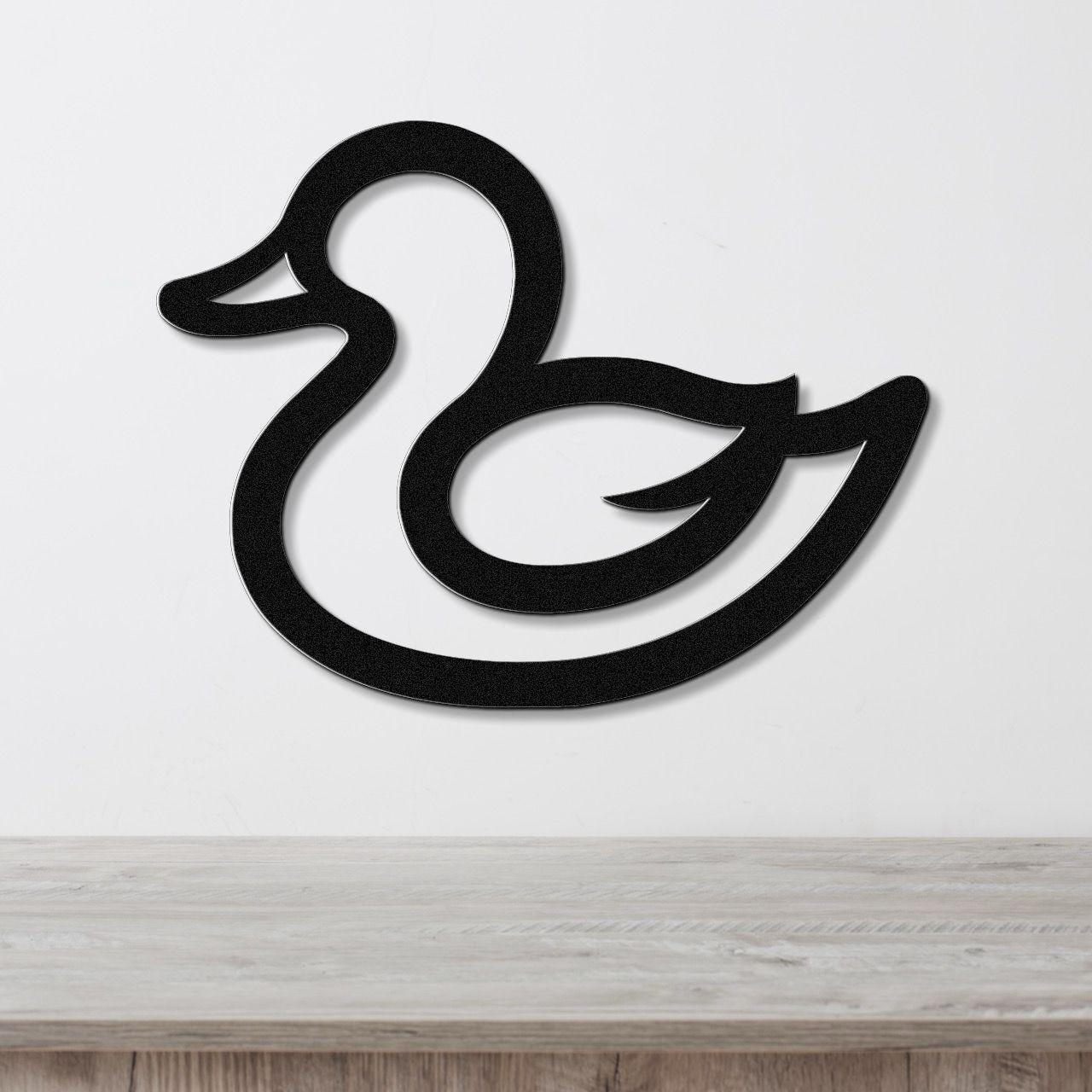 Black metal duck wall art with a silhouette cutout design, mounted on a white wall above a light wood surface.