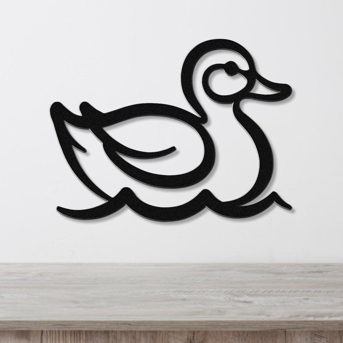Black metal duck wall art with a silhouette design, mounted on a white wall above a light wood surface.