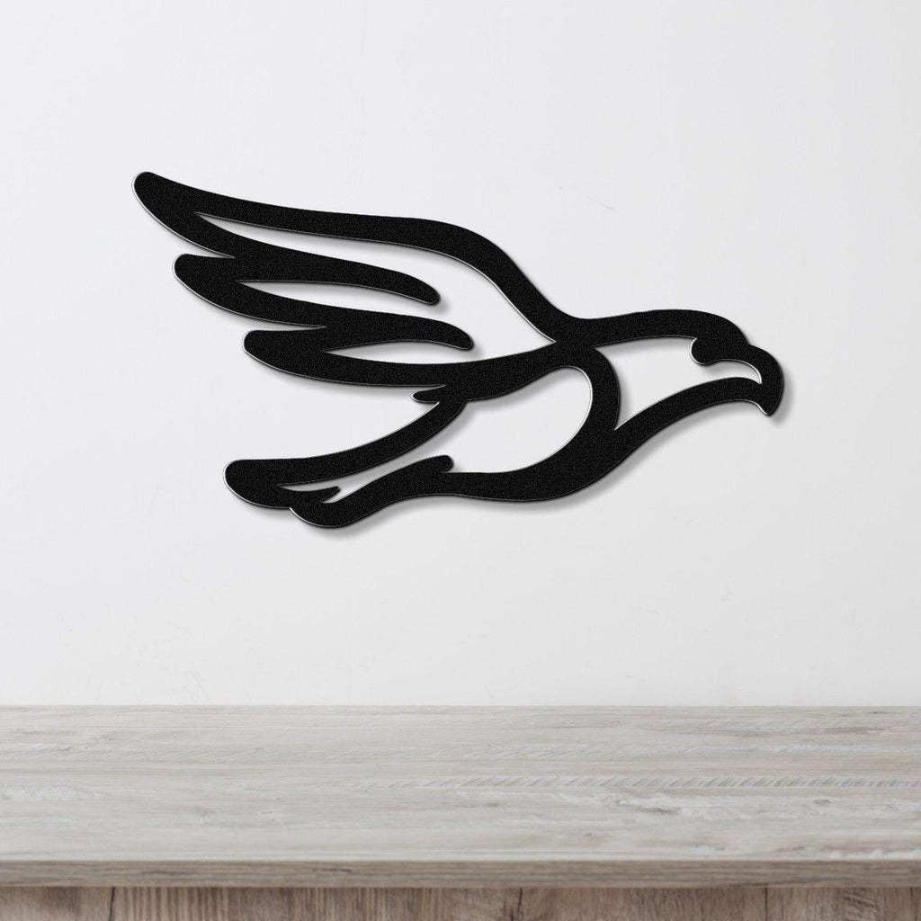 Black metal eagle wall art with a bold silhouette and wing cutouts, mounted on a white wall above a light wood surface.